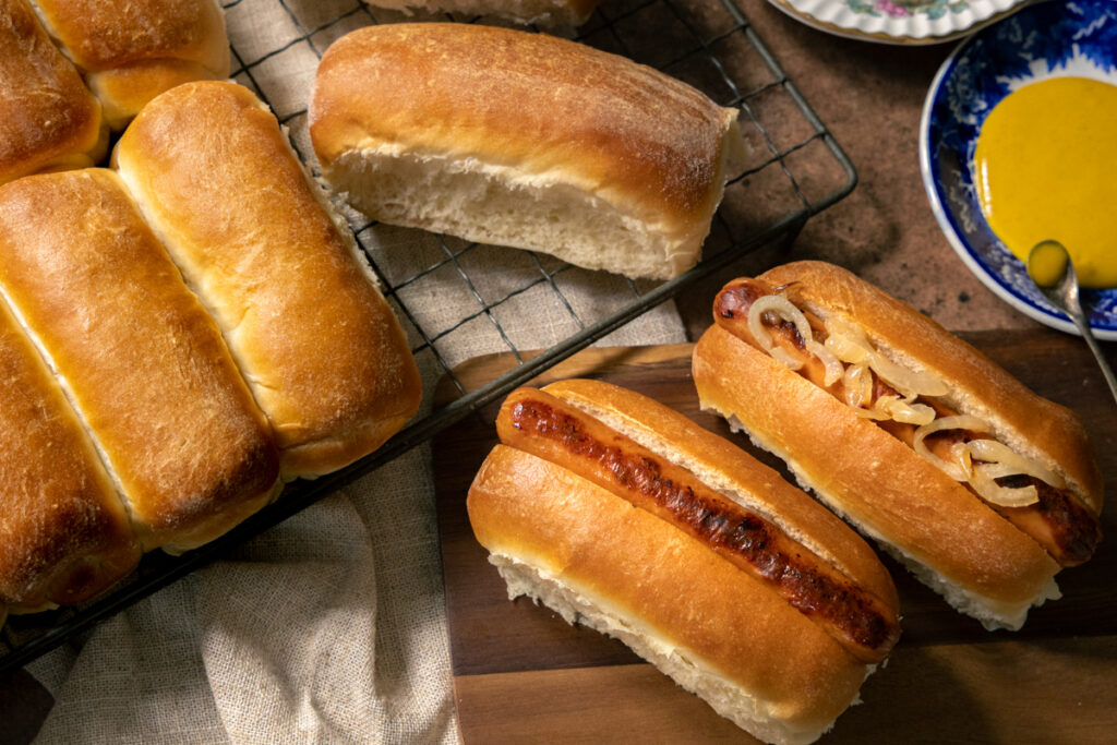 freshly baked homemdae hotdog rolls filled with sausages and fried onions