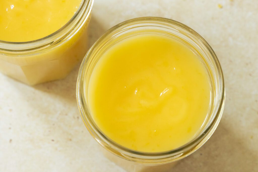 lemon curd recipe A top-down view looking into an open glass jar of smooth, vibrant yellow homemade lemon curd, showing a glossy emulsion