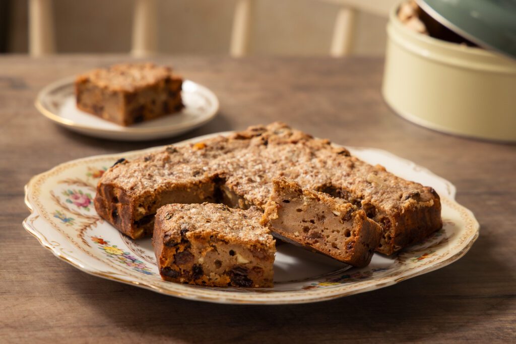 Classic old fashioned bread pudding sliced on a vintage floral plate, showing its golden-brown crust and moist fruit-filled interior, photographed on a rustic wooden table for The Thrifty Squirrels homemade bread pudding recipe.