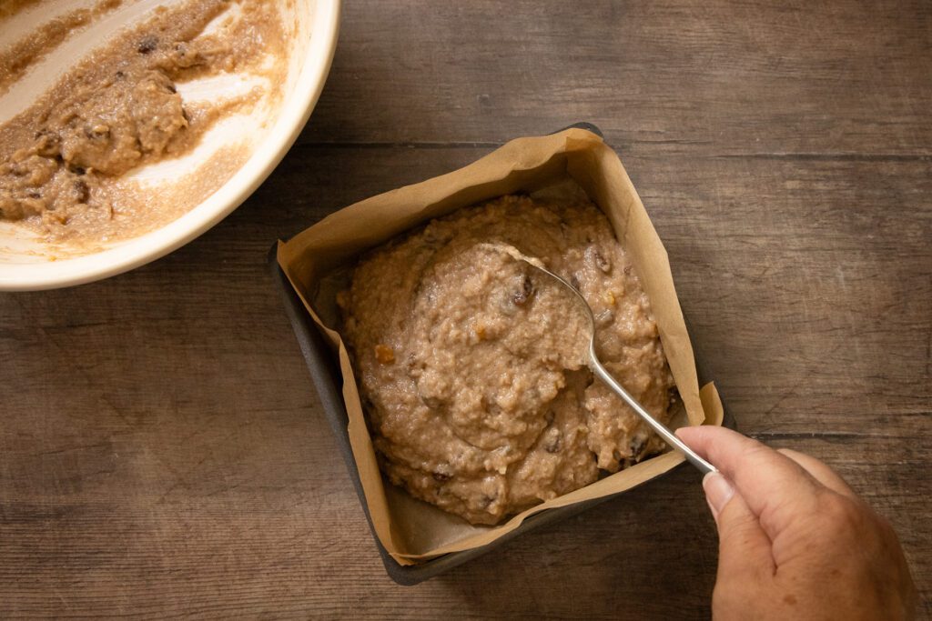 classic old fashioned bread pudding recipe spooning the mixture into a cake tin ready to bake
